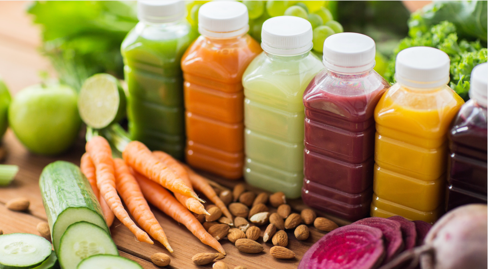 Different colored drinks surrounded by fruits and vegetables you can use for juicing.